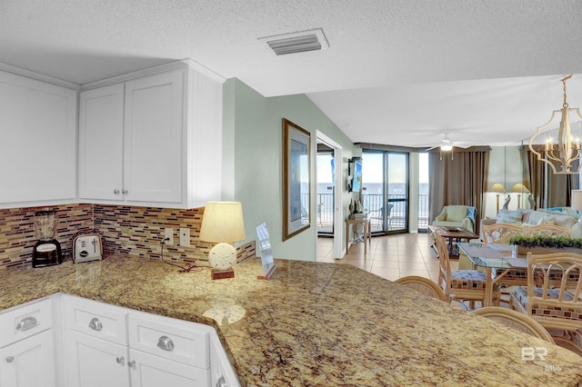 kitchen with a textured ceiling, white cabinetry, light tile patterned flooring, and backsplash