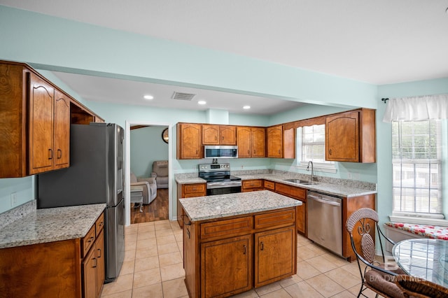 2553 Santa Rosa Dr, Lillian, AL 36549 - kitchen featuring stainless steel appliances, a sink, brown cabinetry, a kitchen island, and light tile patterned flooring