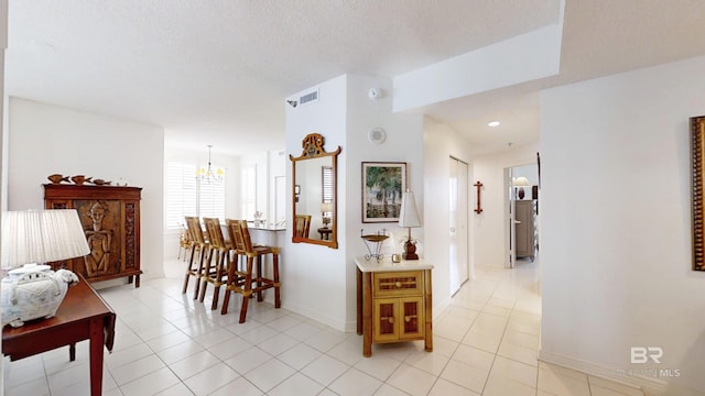 hall featuring light tile patterned flooring, a notable chandelier, and a textured ceiling