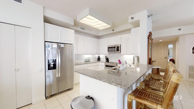 kitchen with a breakfast bar, tasteful backsplash, white cabinets, kitchen peninsula, and stainless steel appliances