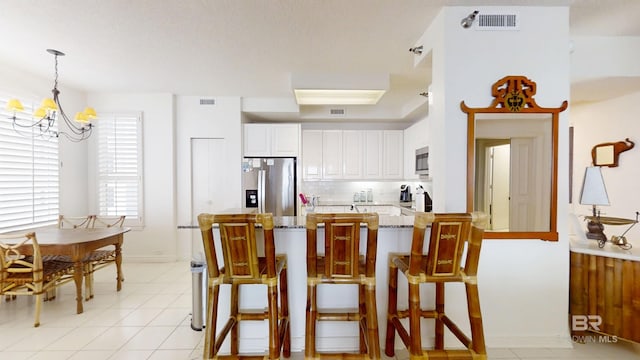 kitchen featuring appliances with stainless steel finishes, a breakfast bar, decorative light fixtures, white cabinets, and light stone counters