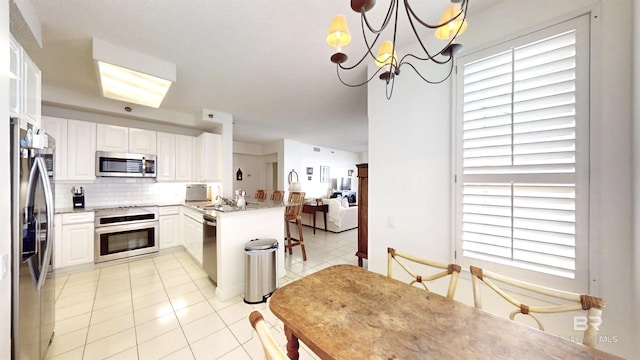 kitchen featuring pendant lighting, white cabinets, decorative backsplash, kitchen peninsula, and stainless steel appliances