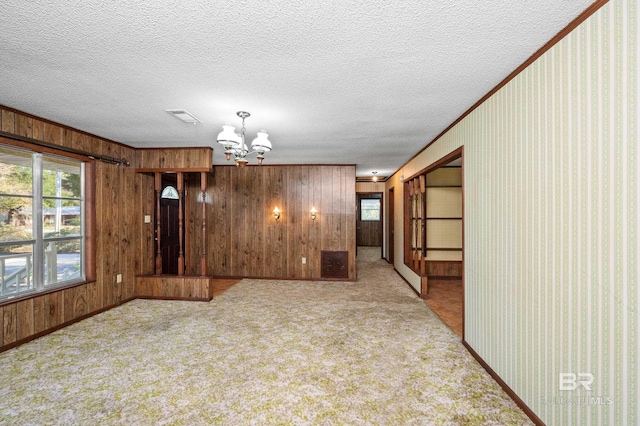 carpeted spare room featuring crown molding, a notable chandelier, a textured ceiling, and wooden walls