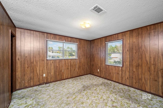 carpeted spare room with a textured ceiling and wooden walls