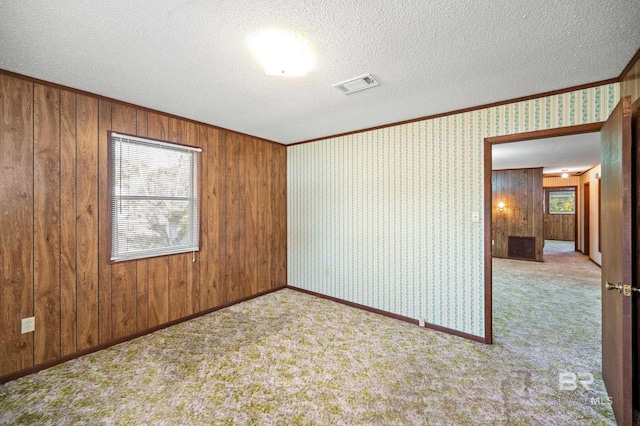 carpeted spare room featuring wood walls, a textured ceiling, and crown molding