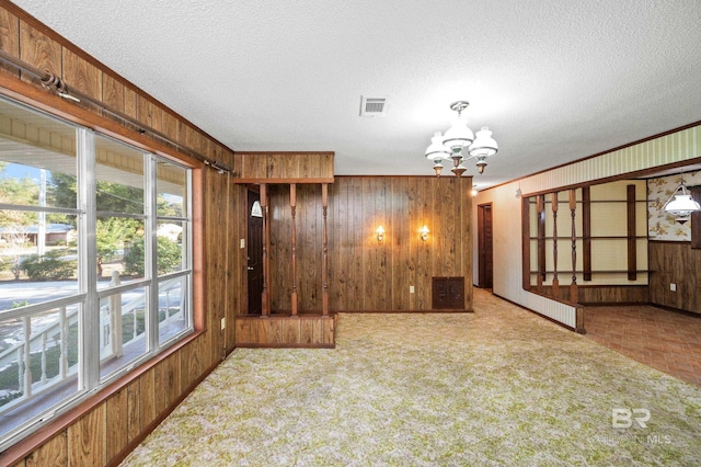 empty room featuring a chandelier, carpet floors, and wood walls