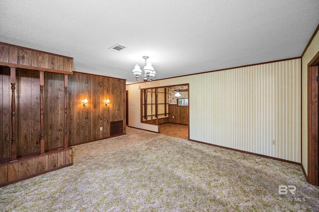 carpeted empty room with ornamental molding, a chandelier, and a textured ceiling