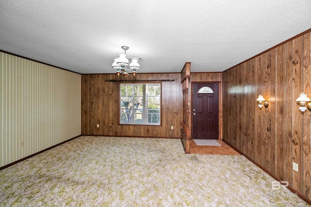 carpeted entrance foyer with crown molding, a notable chandelier, a textured ceiling, and wood walls