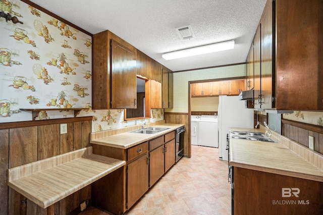 kitchen with black dishwasher, a textured ceiling, washing machine and clothes dryer, wood walls, and sink