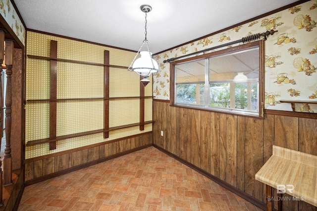 unfurnished dining area with ornamental molding, wood walls, and a textured ceiling