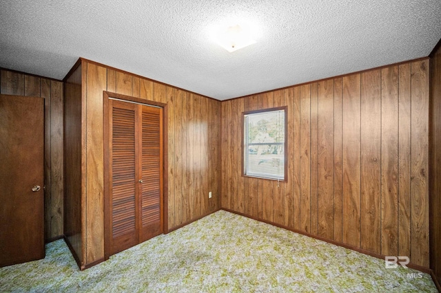 unfurnished bedroom with light carpet, a closet, a textured ceiling, and wooden walls