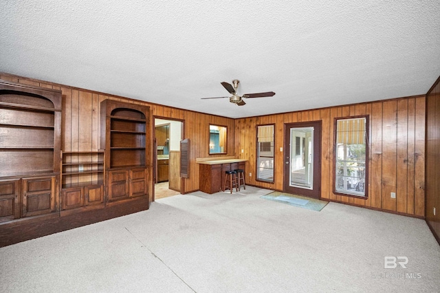 living room featuring wood walls, ceiling fan, light colored carpet, and a textured ceiling