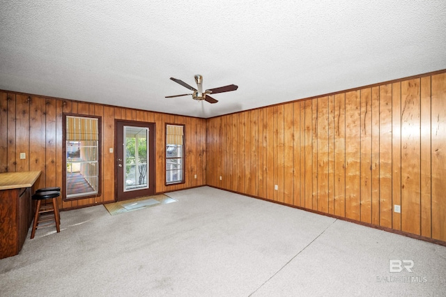 unfurnished living room featuring light carpet, wood walls, a textured ceiling, and ceiling fan