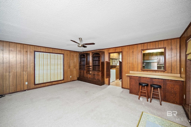 unfurnished living room featuring a textured ceiling, light colored carpet, indoor bar, and wood walls