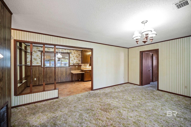 unfurnished room featuring a textured ceiling, wooden walls, crown molding, a chandelier, and light colored carpet