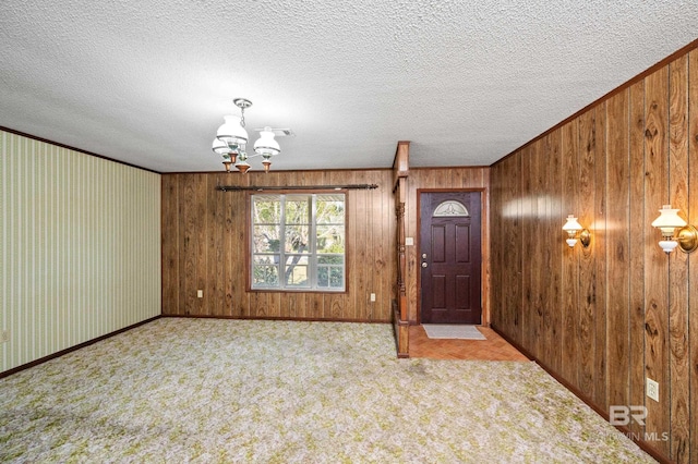 carpeted entrance foyer with ornamental molding, a notable chandelier, a textured ceiling, and wood walls