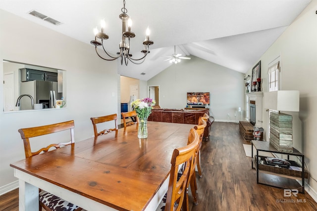 dining room featuring visible vents, a fireplace with raised hearth, lofted ceiling, dark wood-style floors, and ceiling fan with notable chandelier