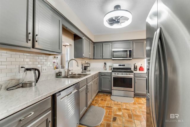 kitchen featuring brick floor, a sink, appliances with stainless steel finishes, gray cabinets, and backsplash