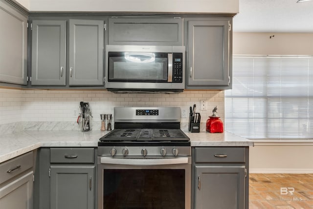 kitchen featuring tasteful backsplash, baseboards, gray cabinets, stainless steel appliances, and light countertops