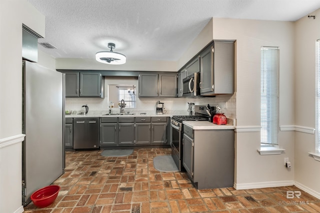 kitchen featuring a sink, light countertops, appliances with stainless steel finishes, gray cabinets, and tasteful backsplash