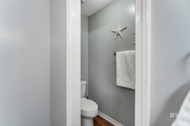 bathroom featuring toilet, baseboards, a textured ceiling, and wood finished floors