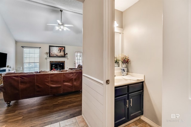 interior space with lofted ceiling, a tile fireplace, wood finished floors, a ceiling fan, and wainscoting