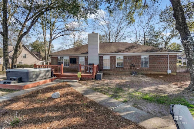 rear view of property featuring a deck, a chimney, brick siding, and a hot tub