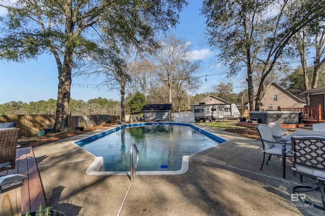 view of pool with a hot tub, a fenced backyard, an outbuilding, a storage unit, and a wooden deck