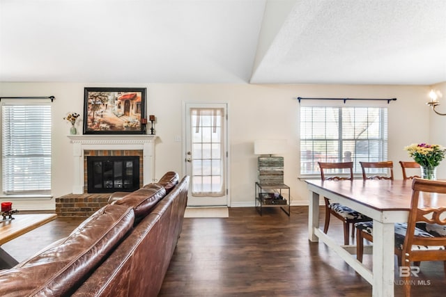 living room with a textured ceiling, a brick fireplace, dark wood finished floors, and baseboards