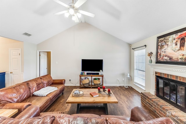 living area with a brick fireplace, visible vents, vaulted ceiling, and wood finished floors