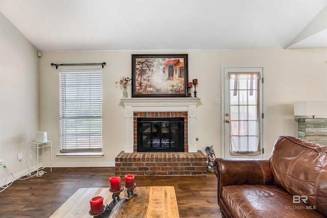 living room with a brick fireplace, vaulted ceiling, baseboards, and wood finished floors