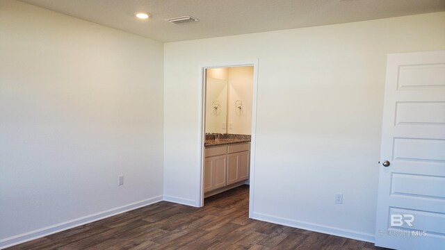 unfurnished bedroom featuring sink, ensuite bathroom, and dark hardwood / wood-style flooring