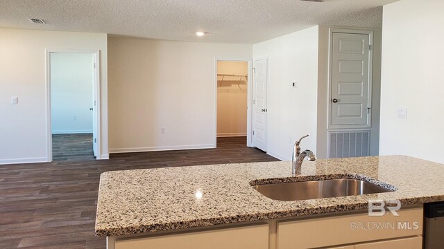 kitchen featuring a textured ceiling, dark wood-type flooring, light stone counters, and sink