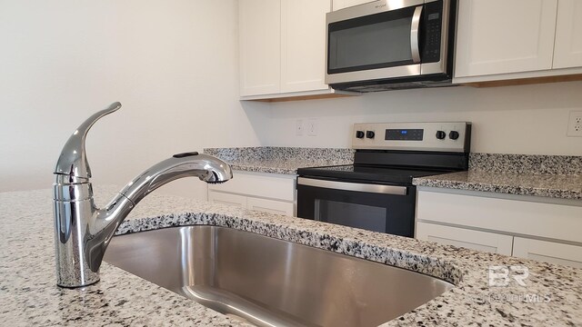 kitchen featuring light stone countertops, white cabinetry, appliances with stainless steel finishes, and sink