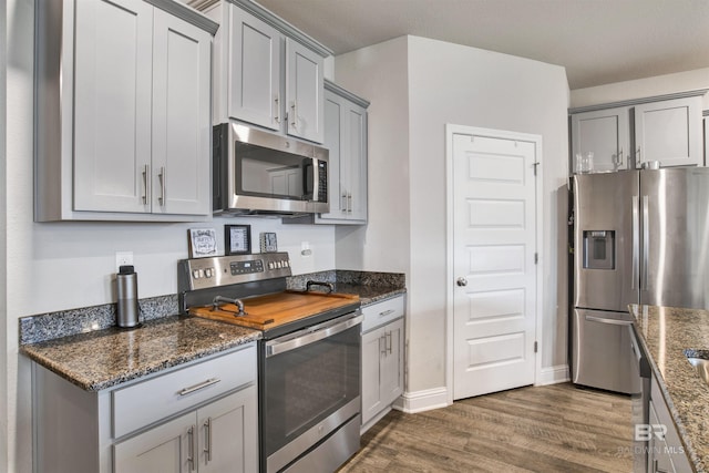 kitchen featuring stainless steel appliances, dark wood-type flooring, gray cabinetry, and dark stone counters