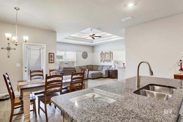 kitchen featuring visible vents, a sink, a raised ceiling, ceiling fan with notable chandelier, and light wood-type flooring