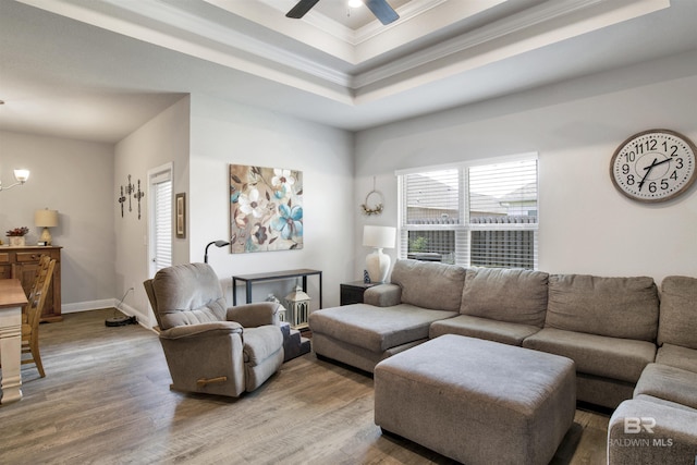 living area with wood finished floors, baseboards, a tray ceiling, crown molding, and ceiling fan with notable chandelier