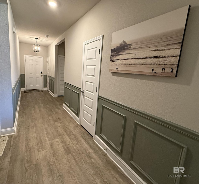 corridor with dark wood finished floors, a decorative wall, and wainscoting