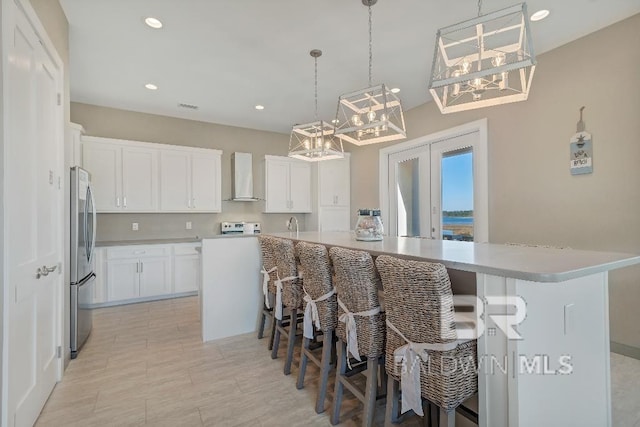 kitchen featuring white cabinetry, wall chimney range hood, a kitchen island with sink, and a breakfast bar area