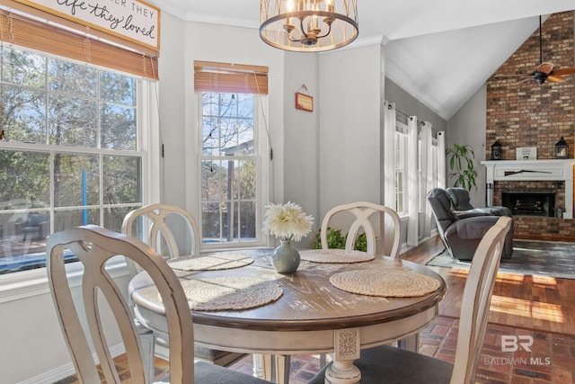 dining room featuring an inviting chandelier, a fireplace, ornamental molding, and vaulted ceiling