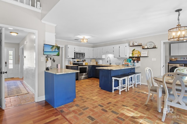 kitchen featuring a kitchen bar, white cabinetry, kitchen peninsula, pendant lighting, and stainless steel appliances