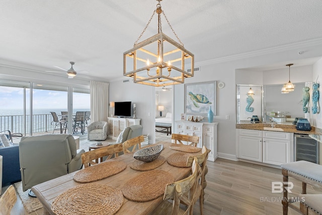 dining room with light wood-type flooring, ceiling fan with notable chandelier, a textured ceiling, beverage cooler, and crown molding