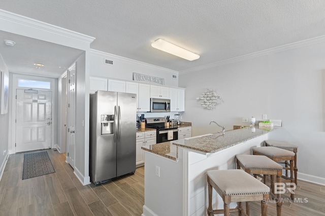 kitchen with kitchen peninsula, appliances with stainless steel finishes, a breakfast bar, light hardwood / wood-style flooring, and white cabinetry