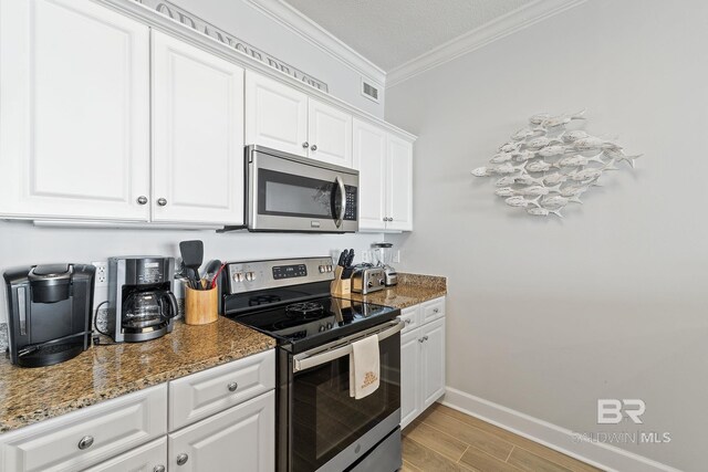 kitchen featuring white cabinetry, light hardwood / wood-style flooring, dark stone counters, and appliances with stainless steel finishes