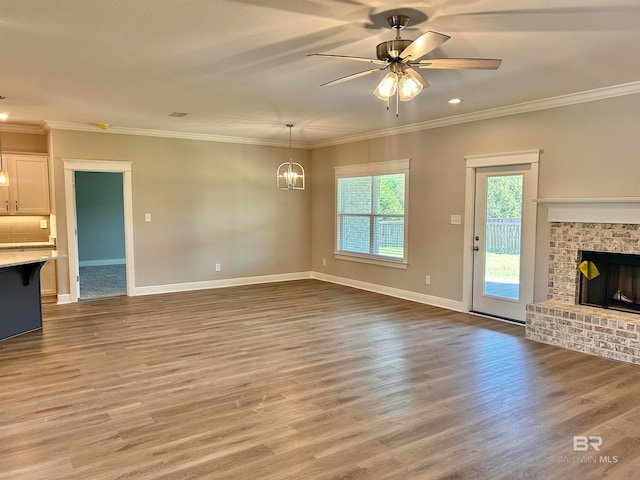 unfurnished living room featuring hardwood / wood-style floors, ornamental molding, and a brick fireplace