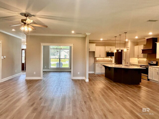 kitchen featuring stainless steel appliances, an island with sink, light hardwood / wood-style floors, decorative light fixtures, and custom range hood