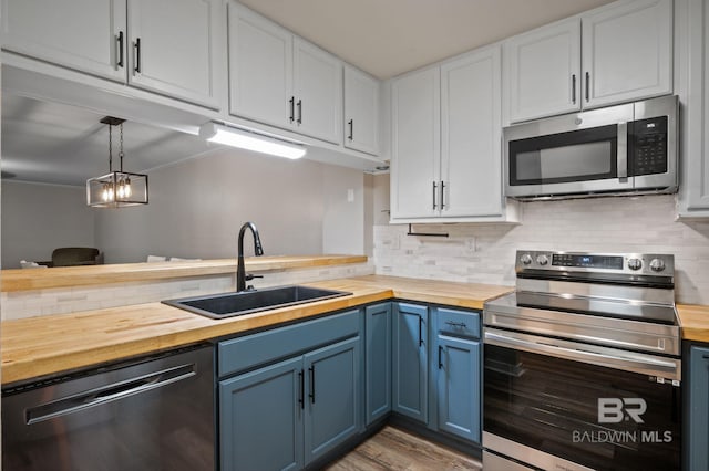 kitchen featuring white cabinets, appliances with stainless steel finishes, butcher block countertops, and decorative light fixtures