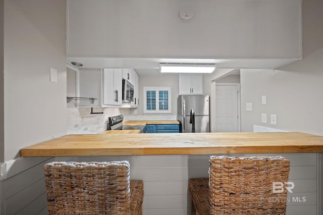 kitchen featuring white cabinetry, butcher block counters, backsplash, and appliances with stainless steel finishes