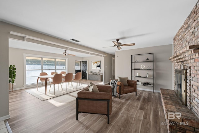 living room with wood-type flooring, a brick fireplace, and ceiling fan