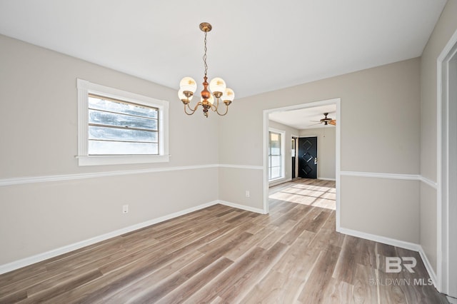 empty room with plenty of natural light, wood-type flooring, and ceiling fan with notable chandelier